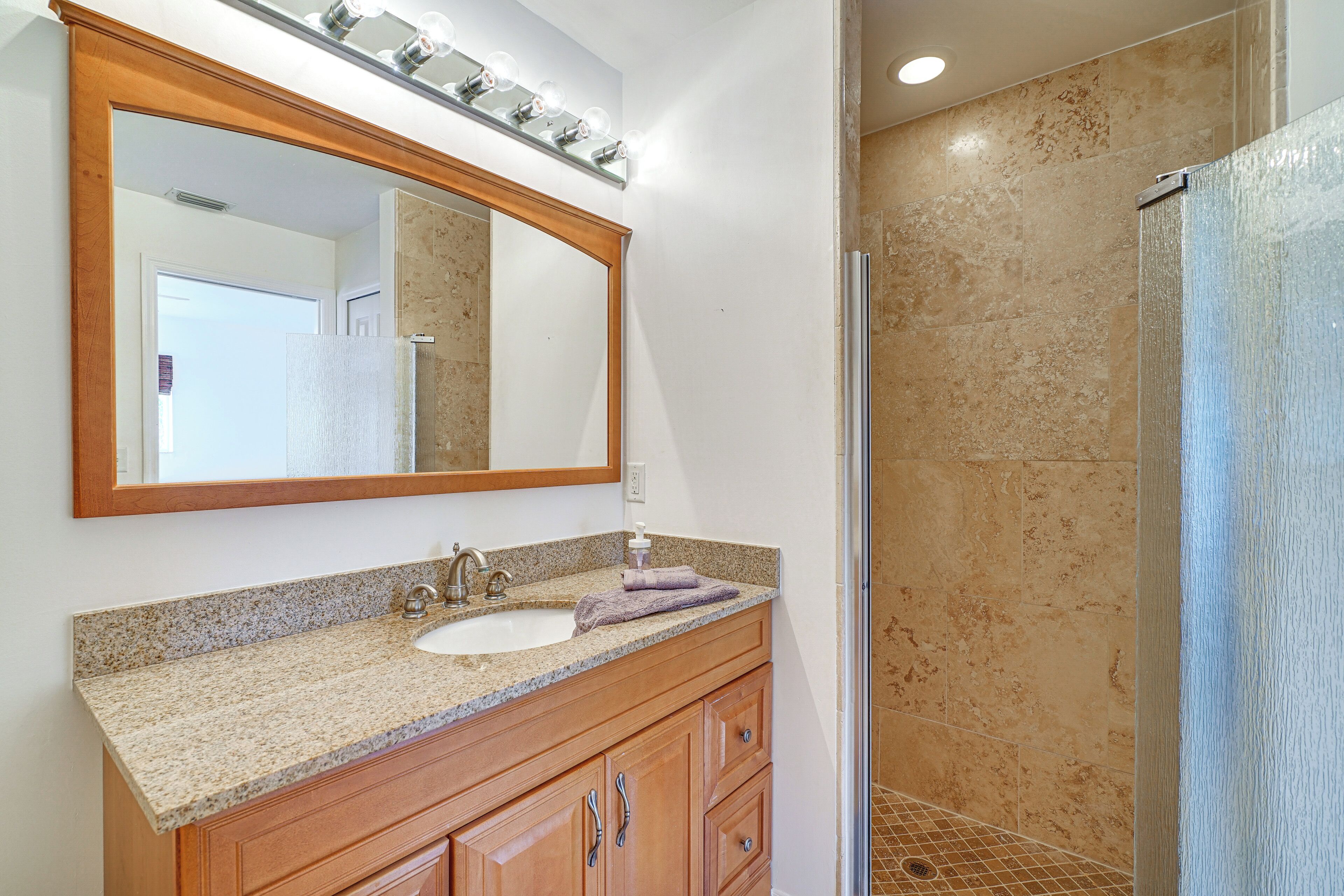 Un baño con lavamanos de encimera de granito, tocador de madera y un espejo grande.