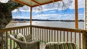 A covered deck with wicker furniture and a view of a lake.