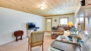 A cozy living room with a television, a dining table with a tray, a striped chair, and a sofa.