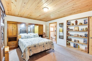 A bedroom with a wooden ceiling, a bed with a beach-themed bedspread, a wooden wardrobe, and a bookshelf with framed photos and books. - Rustic Jefferson Retreat w/ Fire Pit: Near Athens! (Arcade)