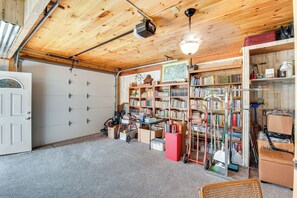 A garage with wooden walls, a ceiling fan, a projector, and shelves filled with books and tools. - Rustic Jefferson Retreat w/ Fire Pit: Near Athens! (Arcade)
