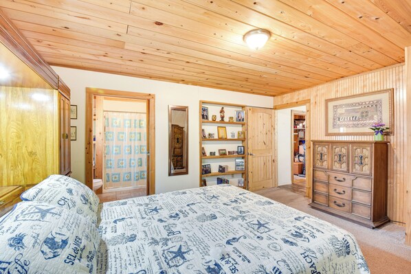 A bedroom with a wooden ceiling, a bed with patterned bedding, a dresser, and a shelf with various items. - Rustic Jefferson Retreat w/ Fire Pit: Near Athens! (Arcade)