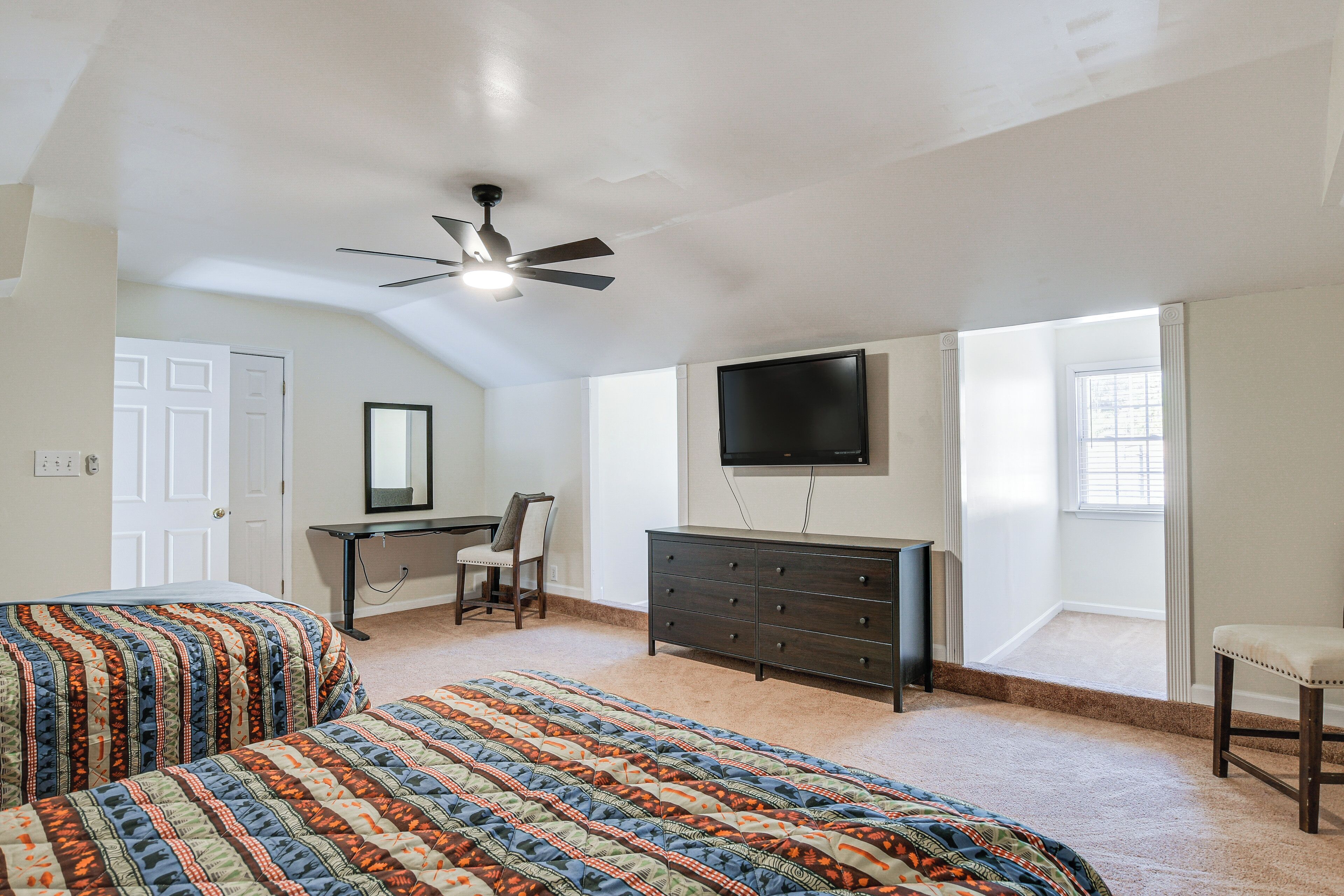 A bedroom with two beds, a desk, a dresser, a TV, and a ceiling fan.