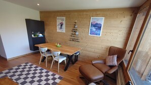 Una habitación acogedora con una mesa de comedor de madera, dos sillas blancas, un sofá de cuero marrón y un pequeño mueble de madera.