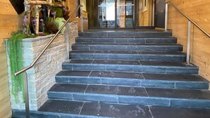 Una escalera conduce a un área de recepción con una lámpara de araña moderna, paredes de madera y una pared de piedra con plantas.