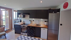 Una cocina compacta con armarios oscuros, un refrigerador de acero inoxidable, un microondas, un lavavajillas y una encimera de madera.