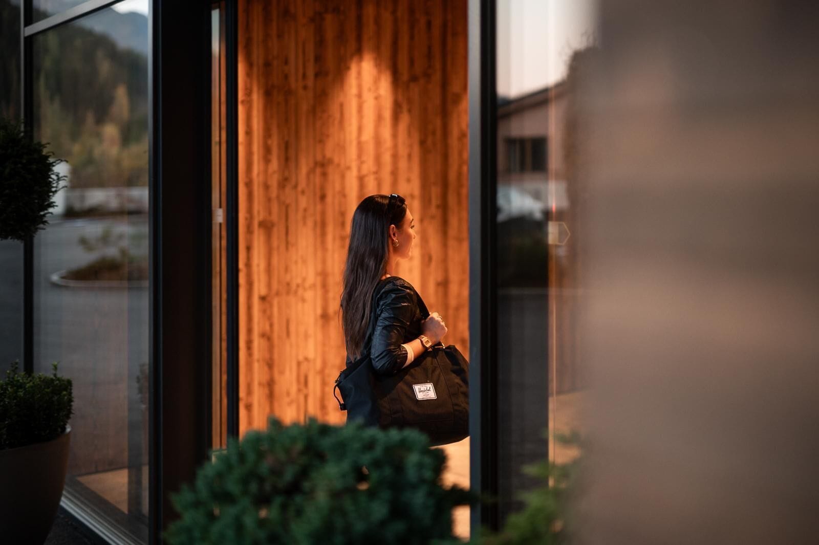 A person standing at the entrance of a building with a wooden interior and glass doors.