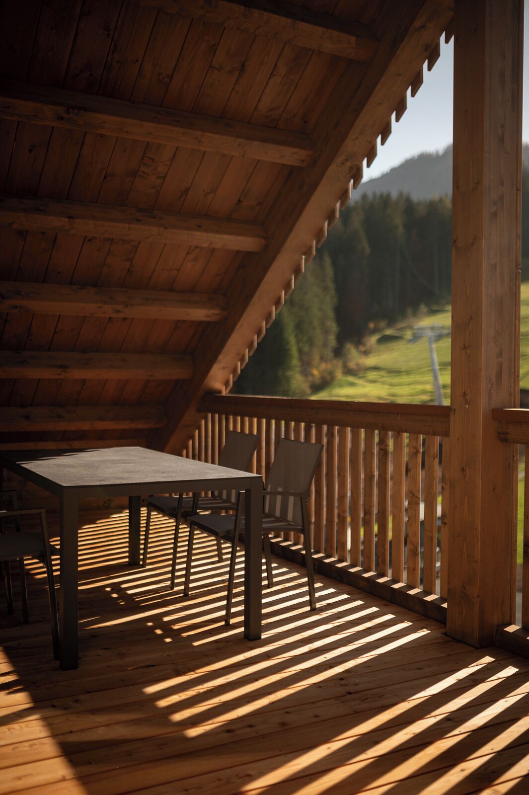 A wooden deck with a table and chairs, overlooking a green landscape.