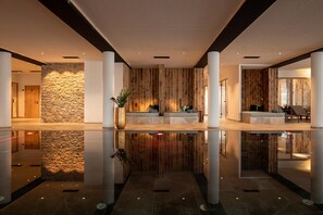 Ruime lobby met een spiegelende vloer, een stenen muur, houten lambrisering en een receptiegedeelte met zitplaatsen.