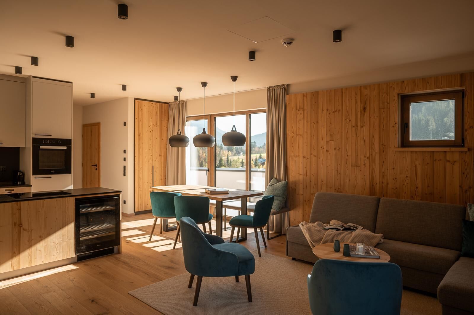 Ein modernes Wohnzimmer mit einer Holzvertäfelung, einem Essbereich mit Stühlen, einem Sofa und einer Küche mit einem Backofen.