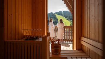 A wooden cabin with a sauna area, a wooden deck, and a view of a green hillside.