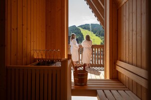 Una cabaña de madera con zona de sauna, una terraza de madera y vistas a una ladera verde.