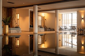 Een moderne hotellobby met een spiegelende vloer, een zithoek met lounge fauteuils en grote ramen die voor natuurlijk licht zorgen.