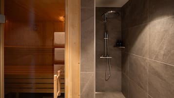 A wooden sauna with a glass door, a shower area with a wall-mounted showerhead, and a small shelf with toiletries.