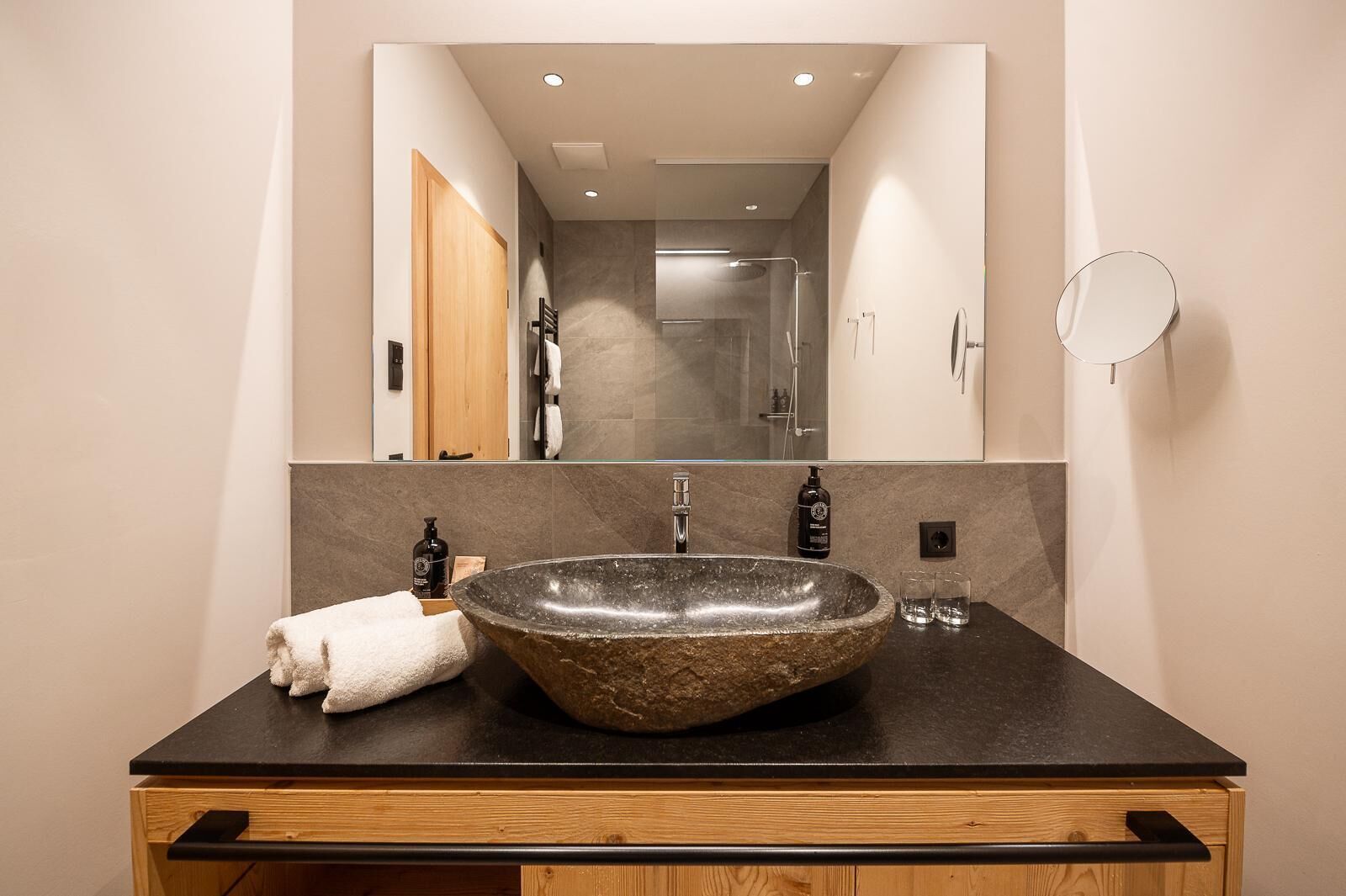 A modern bathroom with a large, oval stone sink, a wooden vanity, a towel, and a mirror.