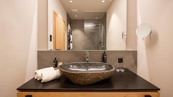Un baño moderno con un lavamanos ovalado de piedra, un mueble de tocador de madera, una toalla y un espejo.