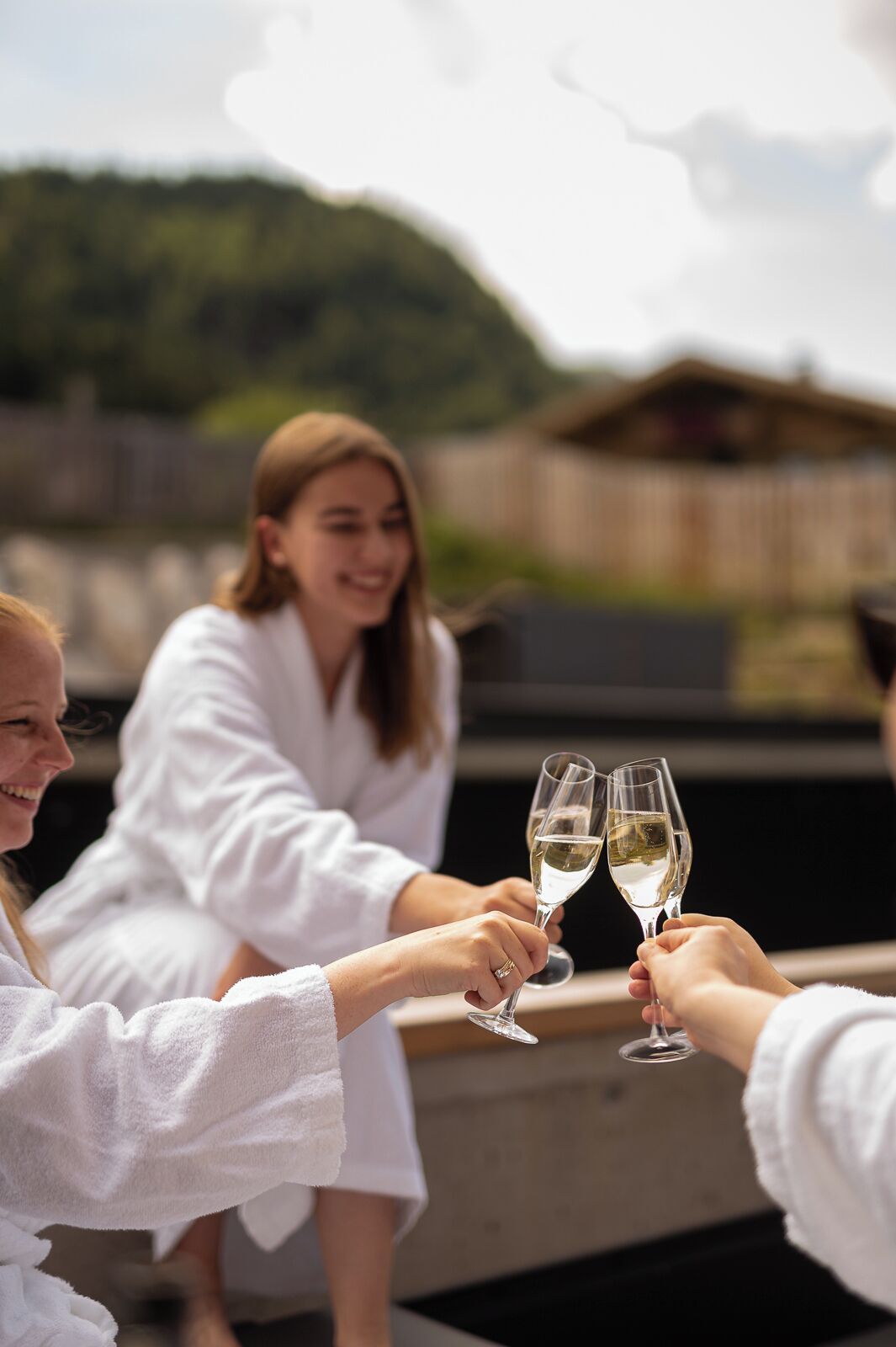 A group of people toasting with champagne glasses on a rooftop terrace with a view of a forested hill in the background.