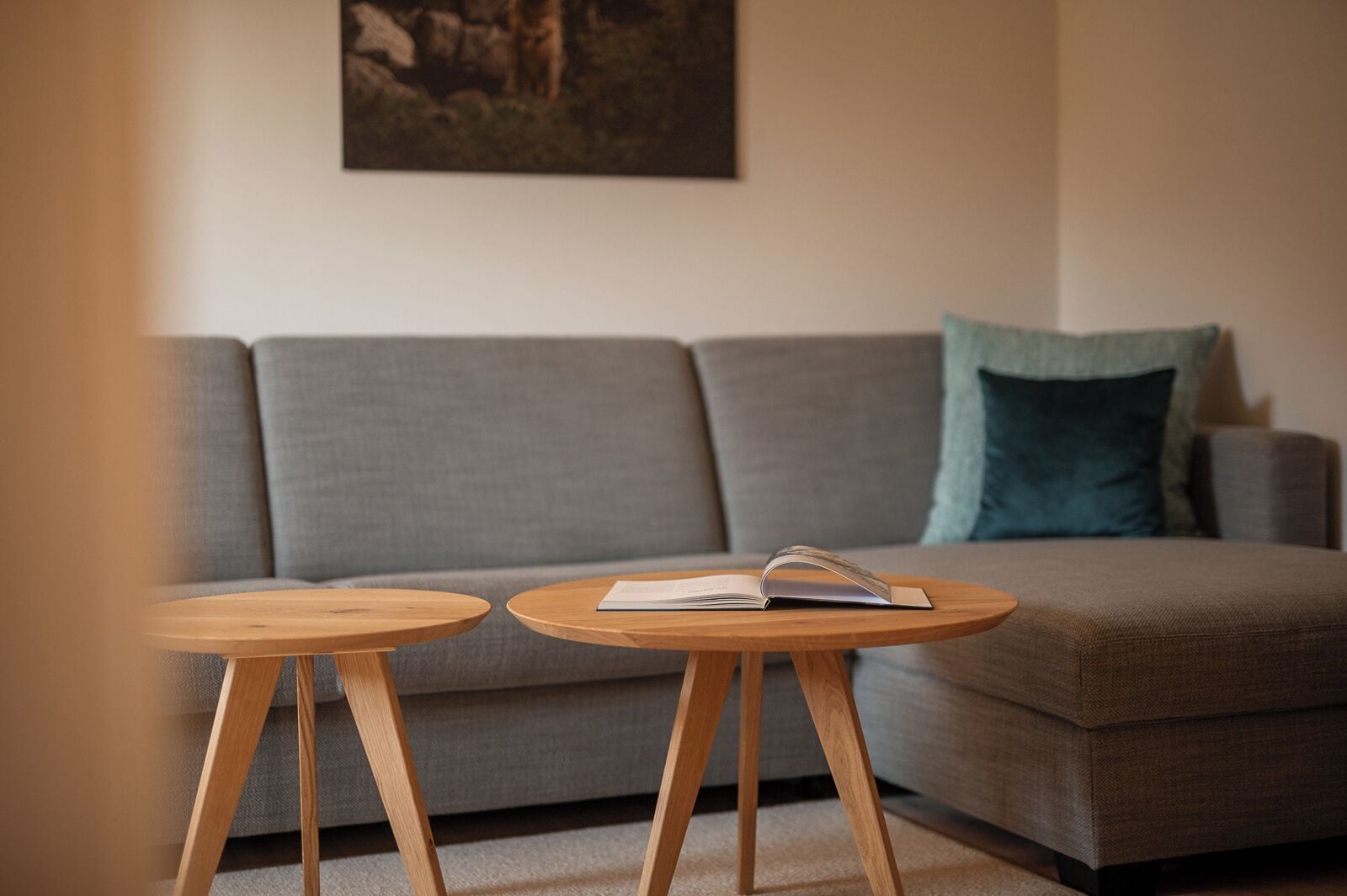 Un salón moderno con un sofá gris, dos mesitas de madera y un libro sobre una de ellas.