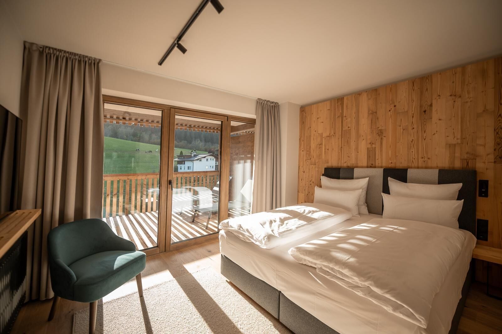 A bedroom with a large bed, a desk, and a view of a wooden deck and green landscape.
