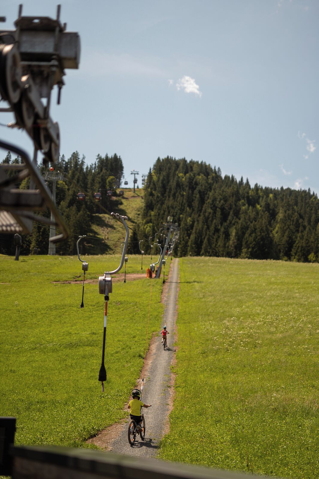 A ski lift with cables and chairs, a clear sky, and a green field with a path.