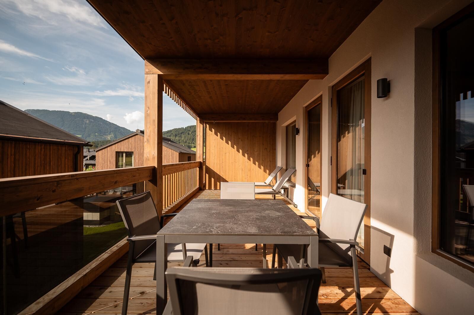 A covered outdoor dining area with a table and chairs, wooden deck, and large windows.