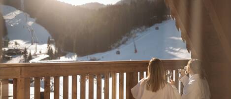 A wooden balcony with a view of a snowy mountain slope and ski lift.