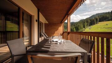 Une terrasse en bois avec une table et des chaises, donnant sur un paysage verdoyant parsemé d’arbres et de collines.