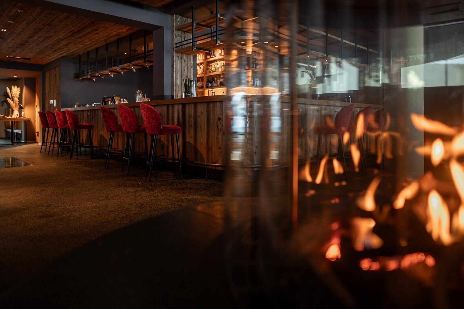 Un espace bar avec des chaises rouges, un comptoir en bois et une cheminée bien visible.
