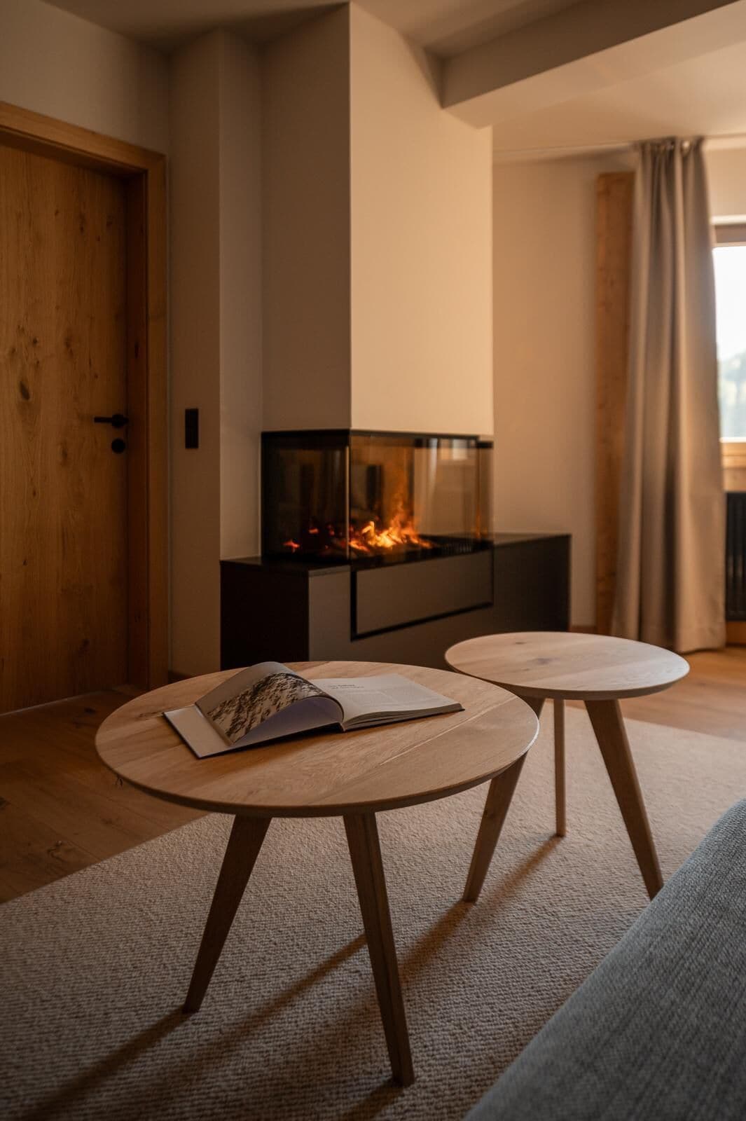 A modern living room with a fireplace, two round wooden tables, and a sofa.
