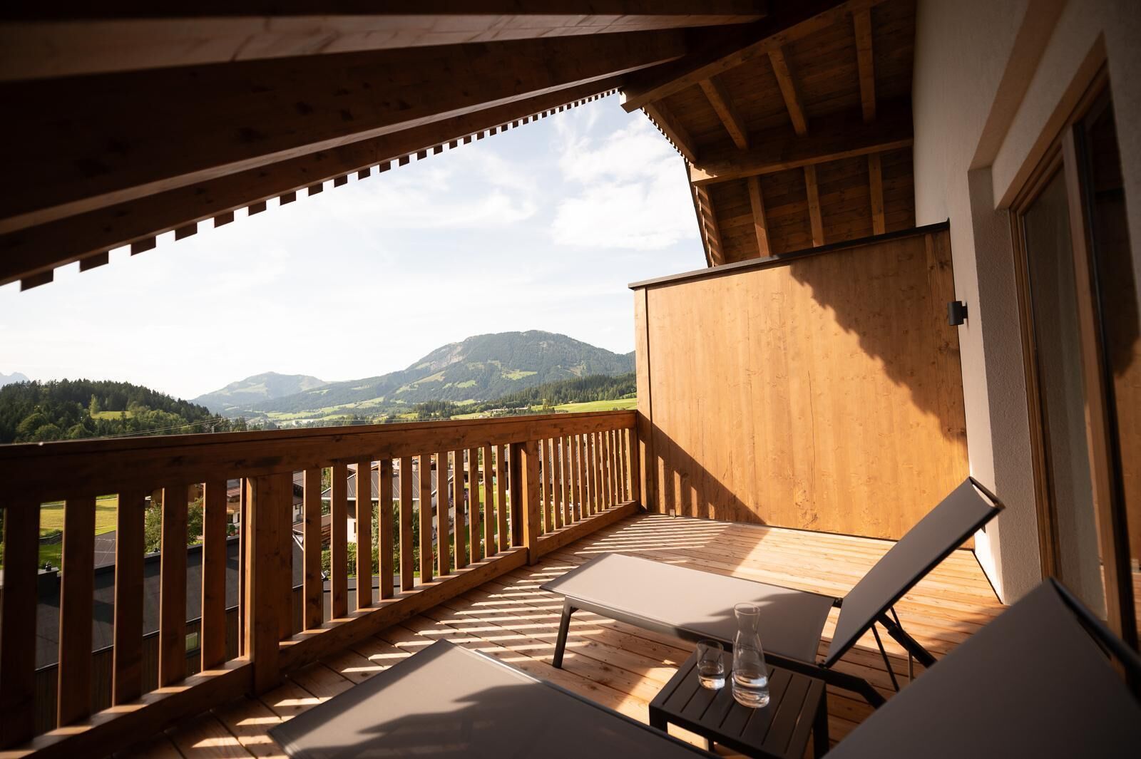 A wooden deck with two lounge chairs and a small table, overlooking a mountainous landscape.