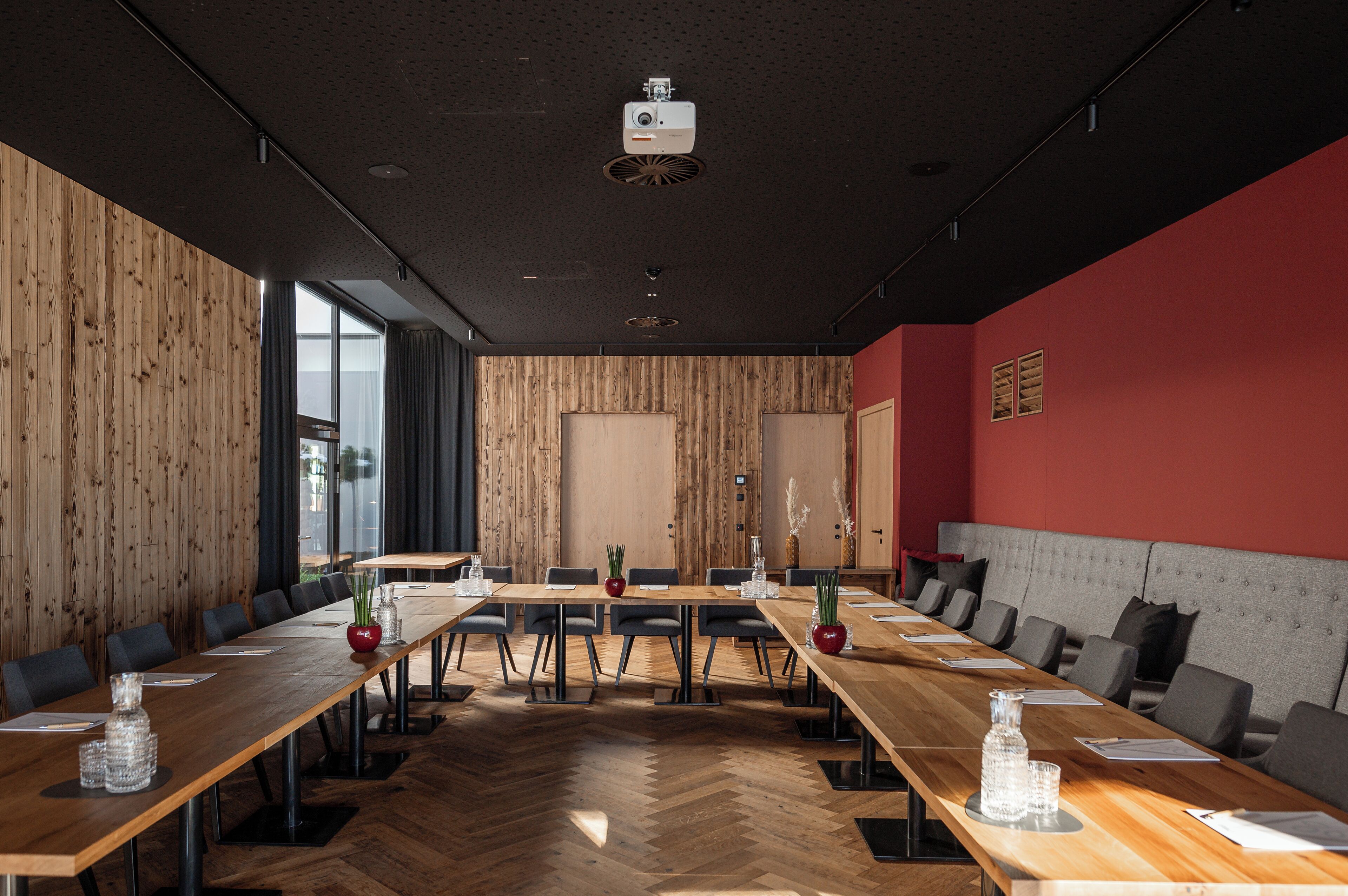 A conference room with a long wooden table, black chairs, and a red accent wall.