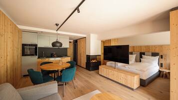 Un espace de vie moderne et compact comprenant un coin cuisine, un espace repas et une chambre dotée d’une grande télévision et d’un lit confortable.