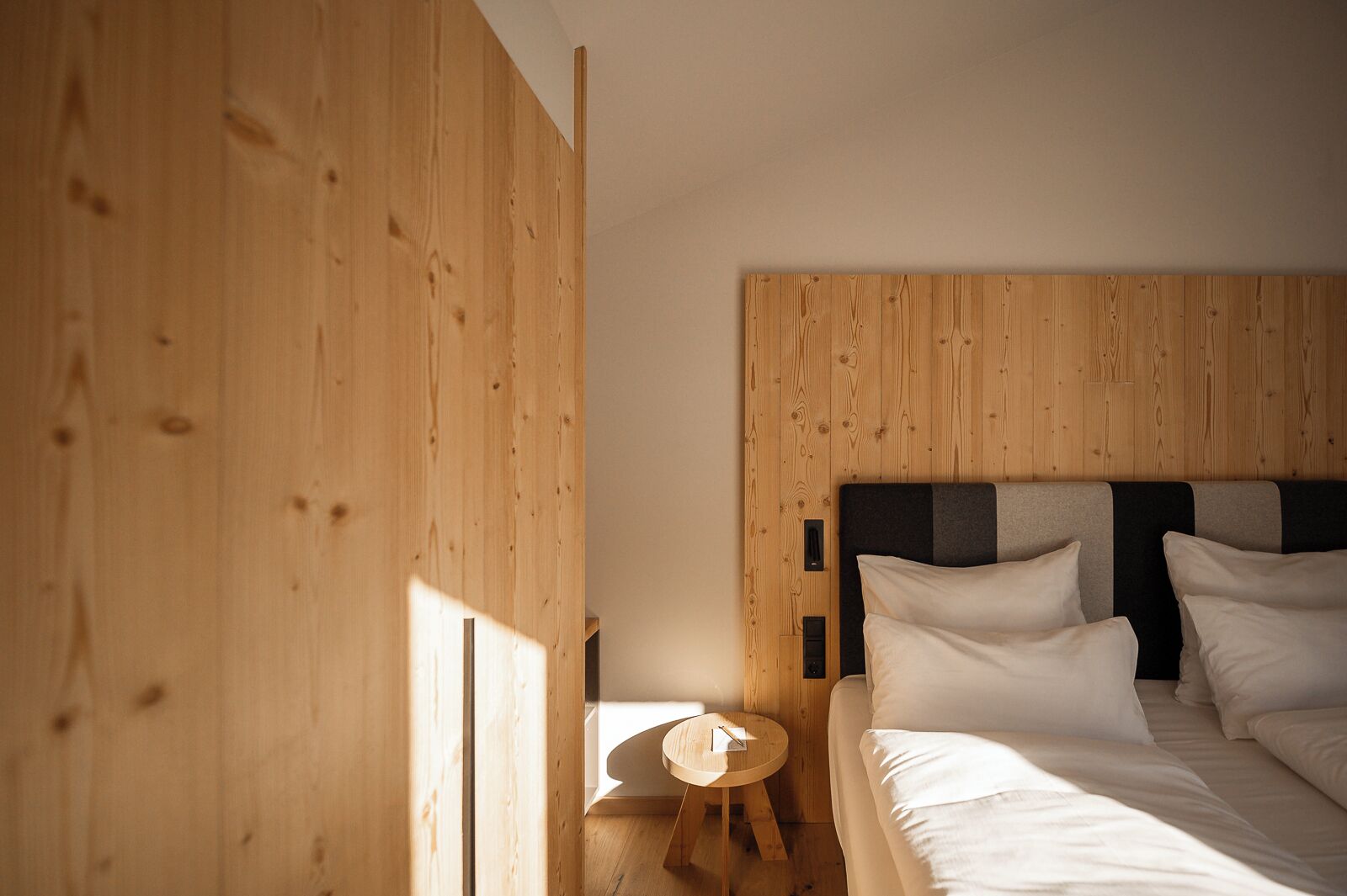 A bedroom with a wooden headboard, a round wooden side table, and a bed with white bedding.