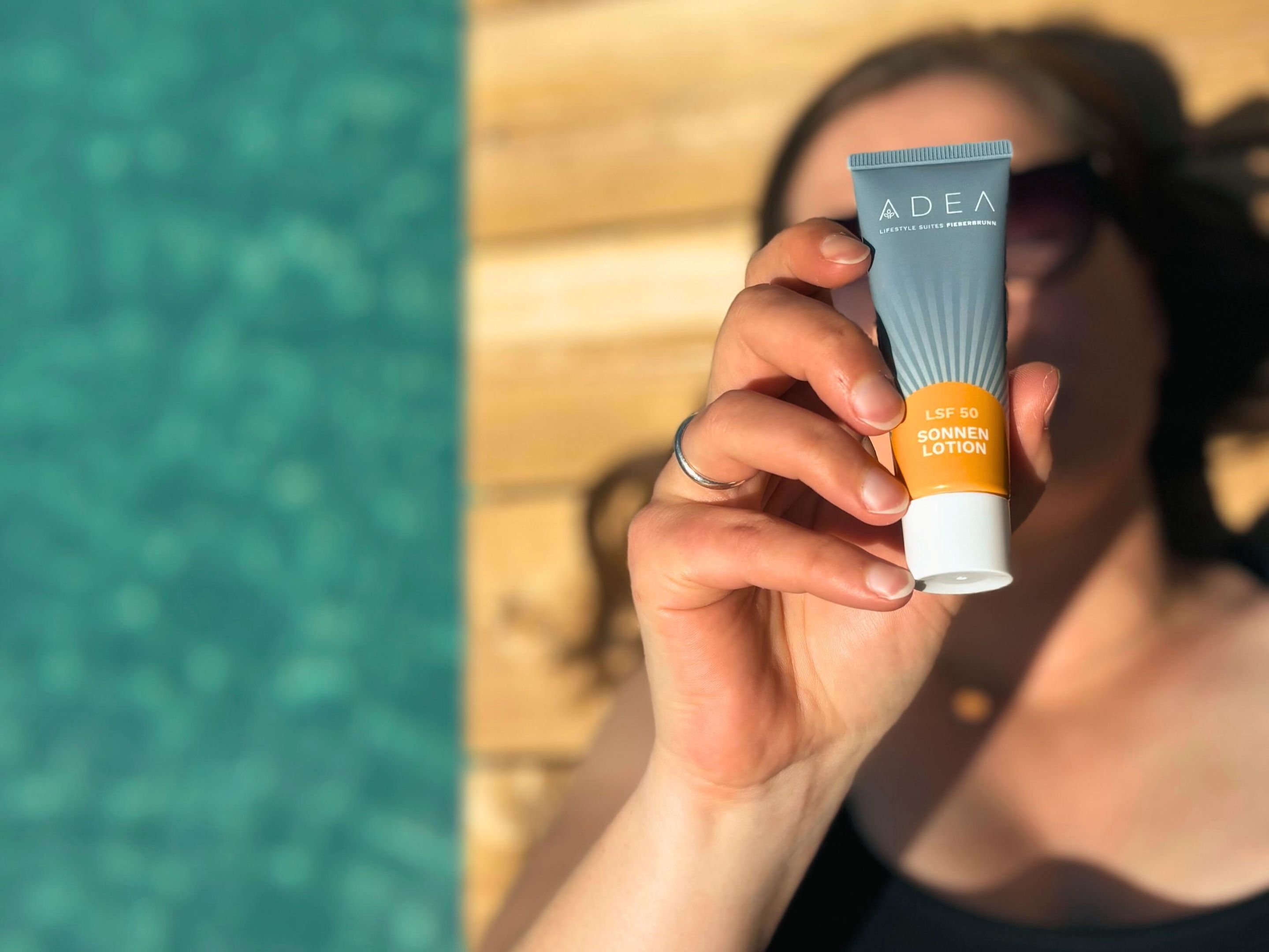 A person holding a sunscreen tube labeled "ADEA LIFESTYLE SUITES FREIBRUNN LSf 50 SONEN LOTION".