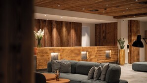 Een moderne receptiezone met een houten receptiebalie, een grijze modulaire bank en een ronde houten tafel met een vaas.