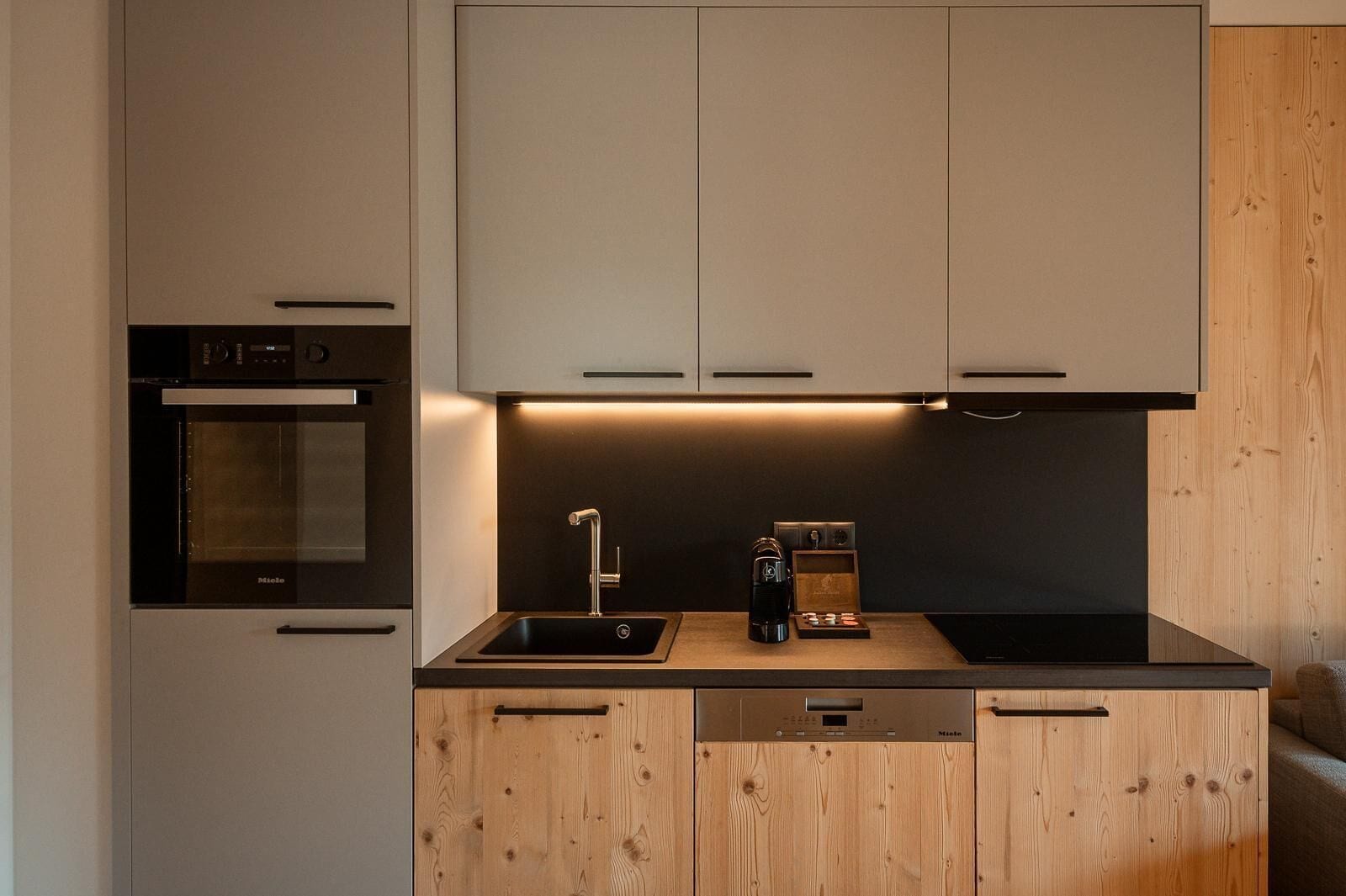 Une cuisine moderne dotée d’un four encastré, d’une machine à café et de meubles de rangement en bois.