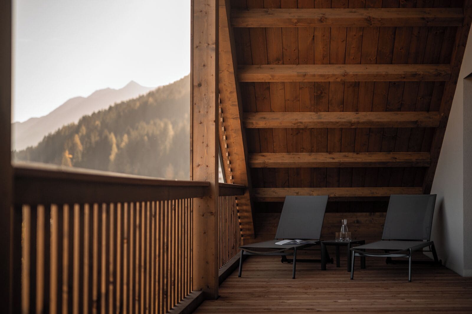 Un balcón de madera con dos sillas y una mesa, con vistas a un paisaje montañoso.