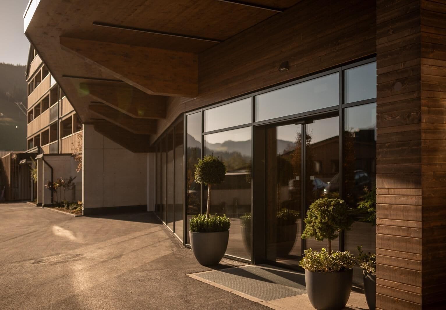 Un edificio moderno con amplios ventanales de vidrio, fachada de concreto y plantas en macetas en la entrada.