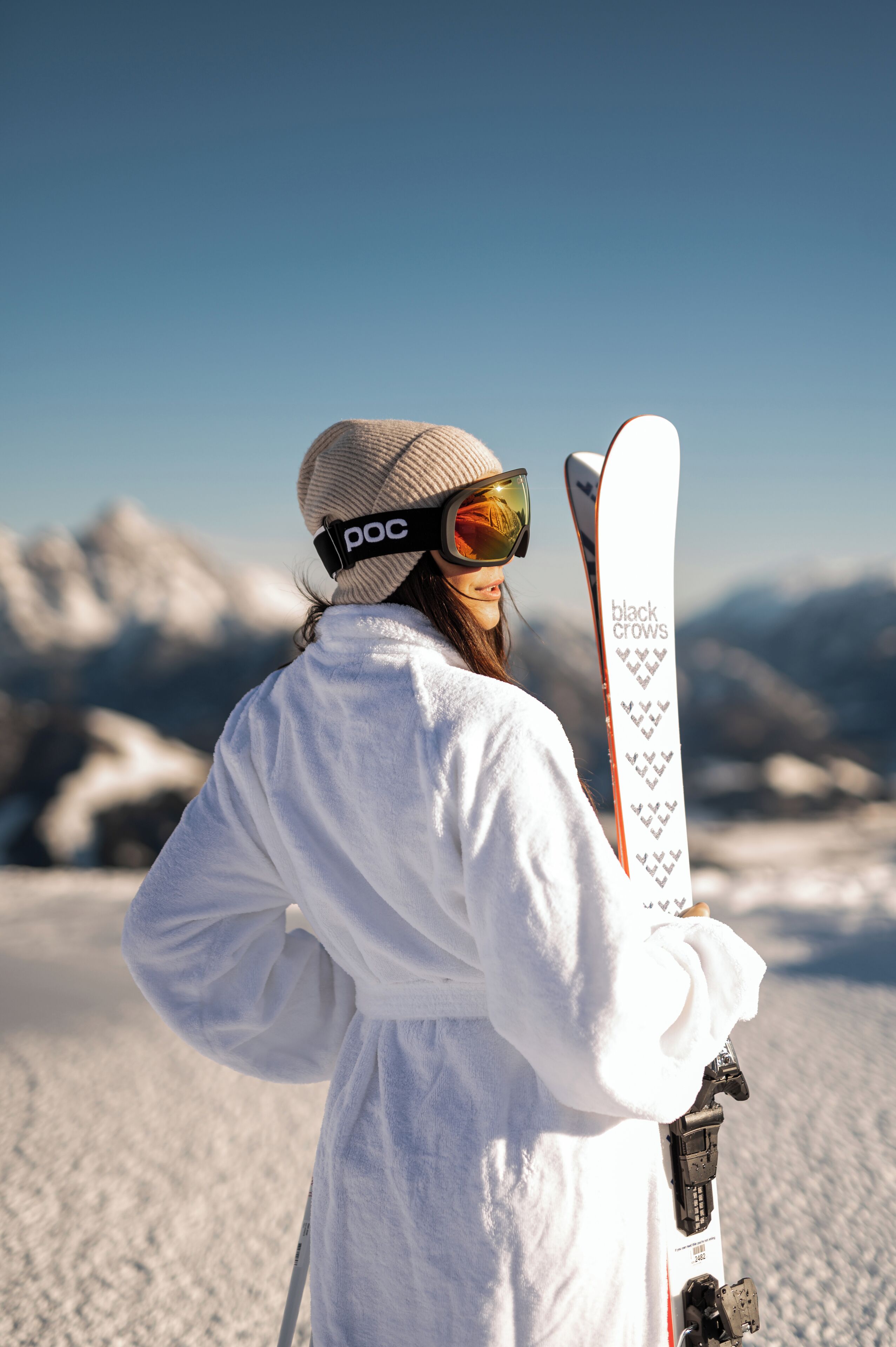 A person with skis and a helmet, standing on a snowy slope with mountains in the background.