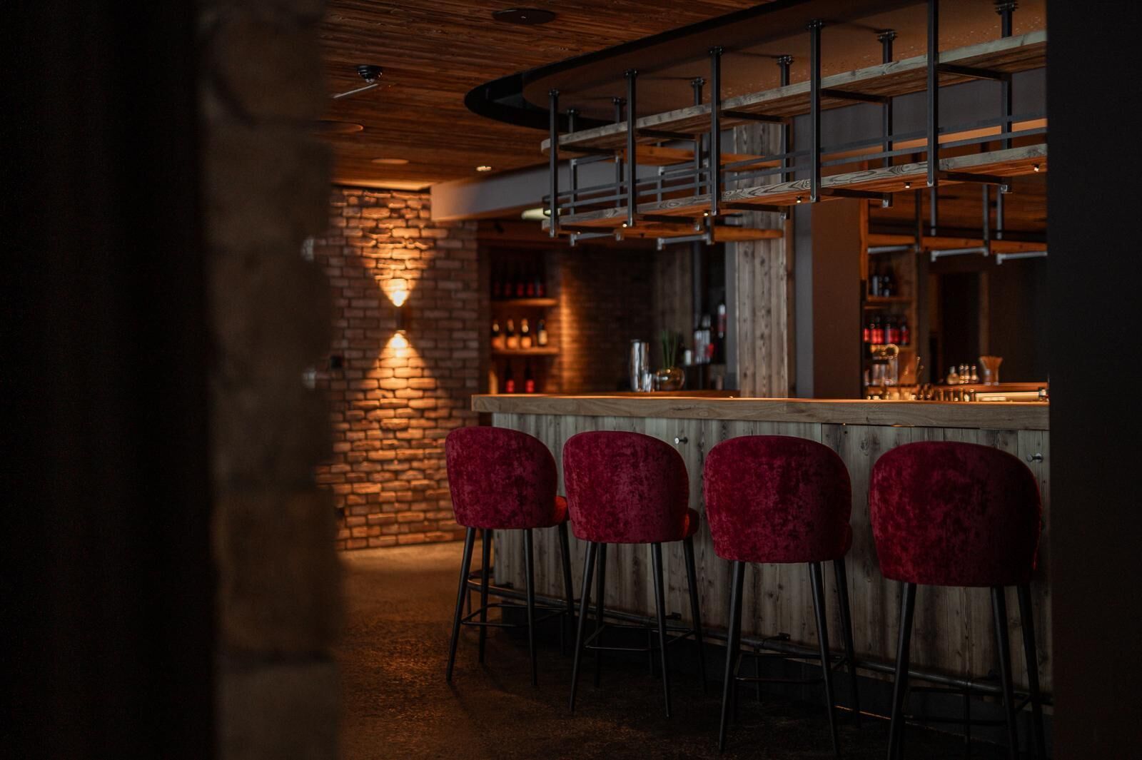 A bar area with a wooden counter, four red bar stools, and a brick wall.
