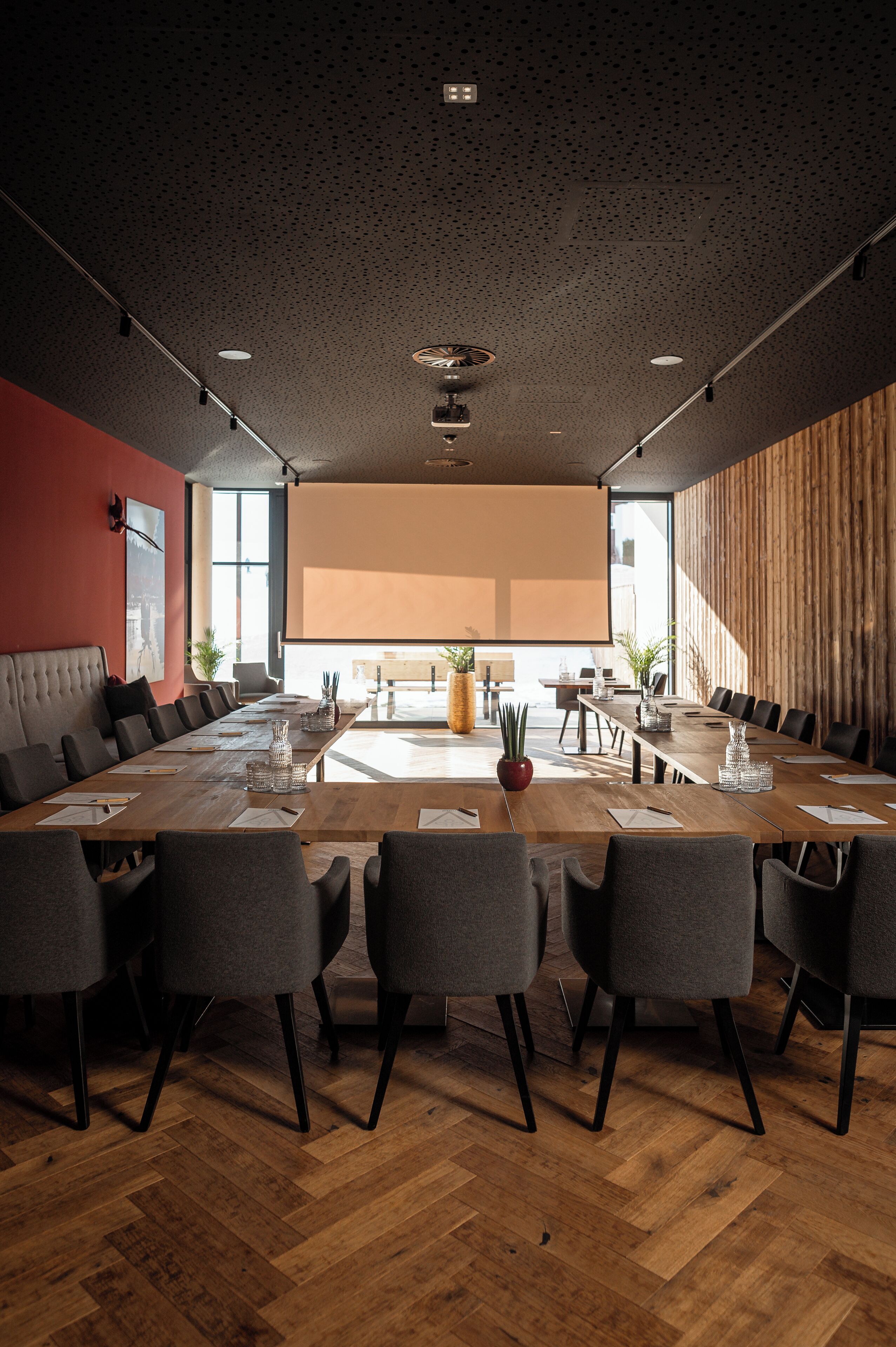 A conference room with a long table, multiple chairs, a projector screen, and a large window.