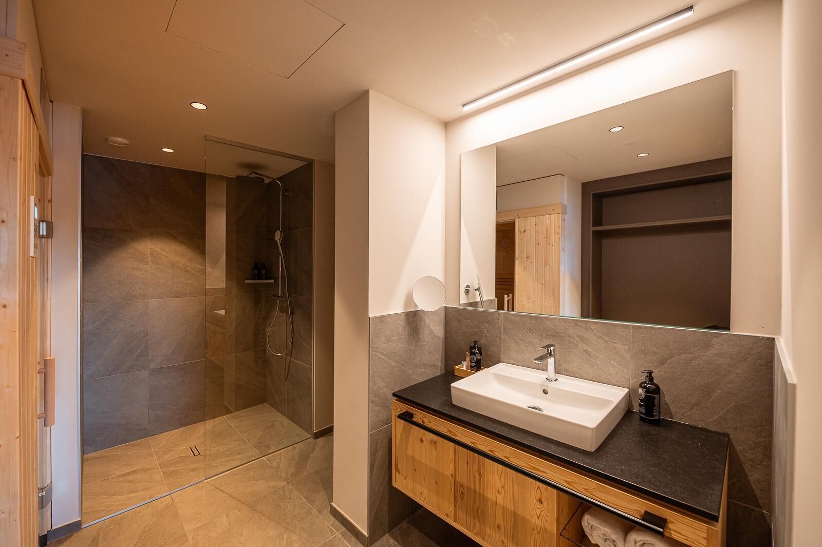 A modern bathroom with a walk-in shower, a large mirror, and a wooden vanity with a sink.