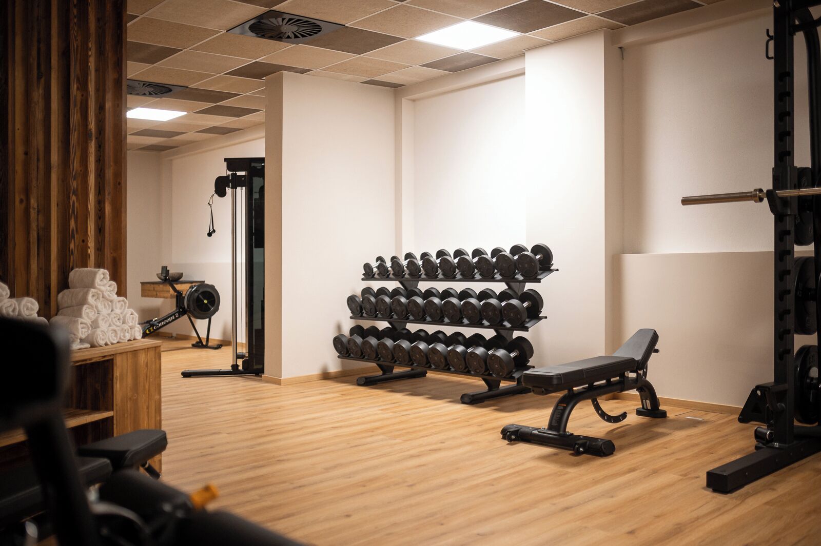 A gym with wooden flooring, a bench, a rack of dumbbells, and a treadmill.