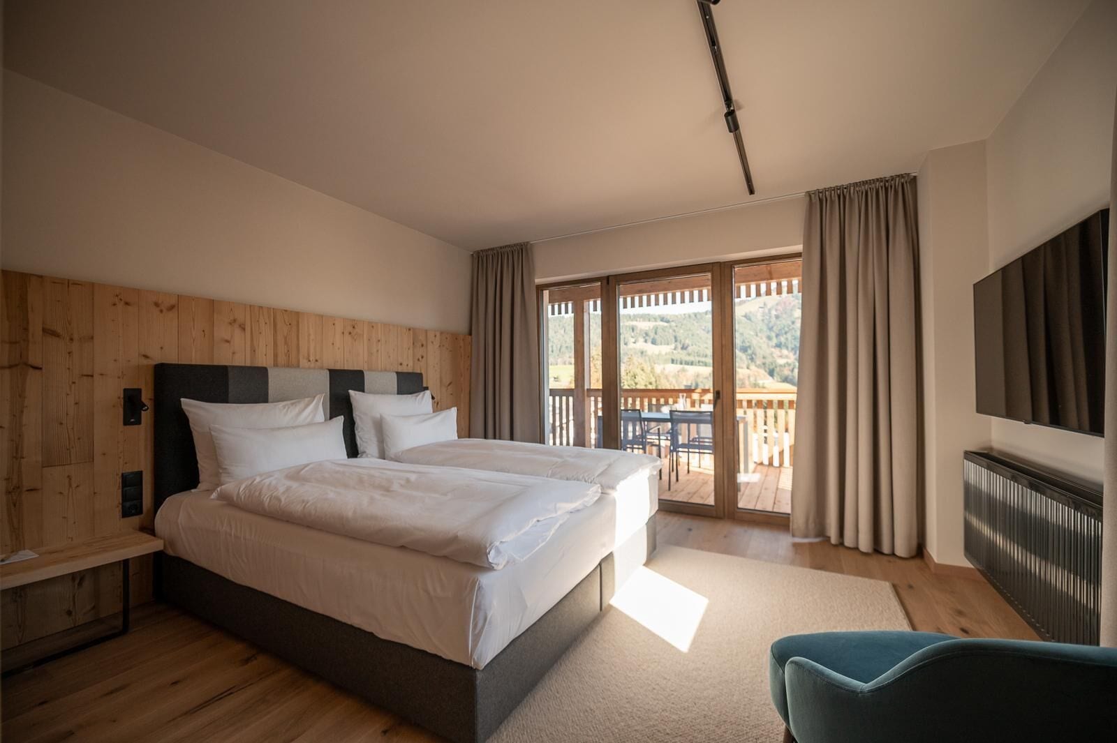 Een tweepersoonsbed met houten hoofdbord, een flatscreen televisie aan de wand en een balkon met tafel en stoelen.
