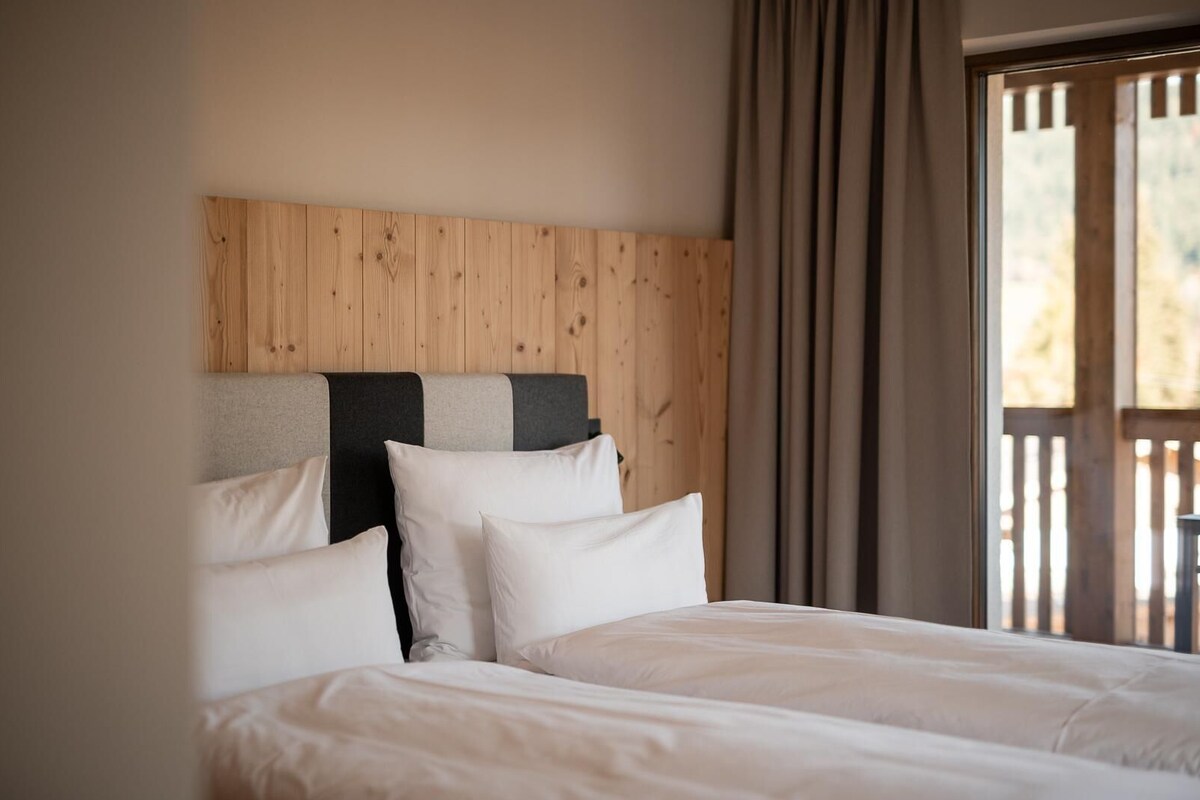 A hotel room with a wooden headboard, two beds, and a view of a wooden deck through a window.
