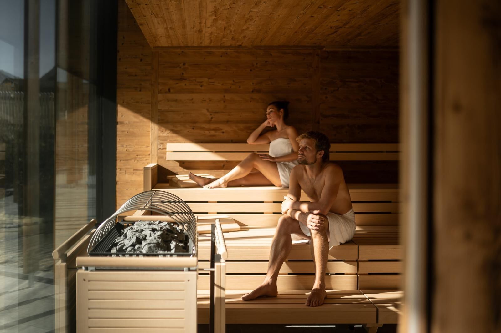A sauna with wooden benches, a charcoal stove, and a glass enclosure.