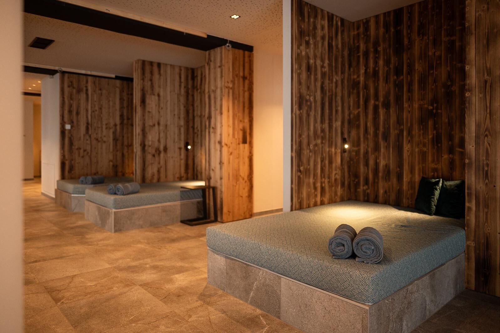 A modern spa room with a large bed, two seating areas, and wooden panel walls.