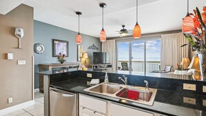 A modern kitchen with a black countertop, stainless steel sink, and overhead pendant lights.