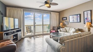 A spacious living room with a large sliding glass door leading to a balcony, a ceiling fan, a television, and a sofa.