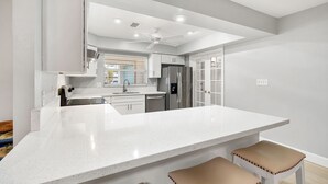 A modern kitchen with a large island, white cabinetry, and a ceiling fan.